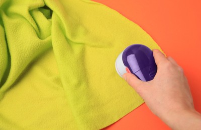Photo of Woman cleaning light green cloth with fabric shaver on orange background, closeup