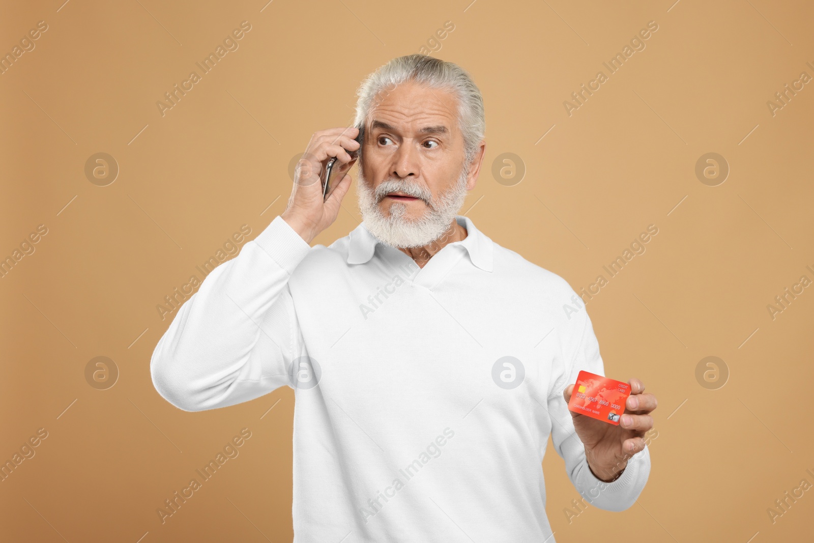 Photo of Senior man with credit card talking on smartphone against beige background. Be careful - fraud