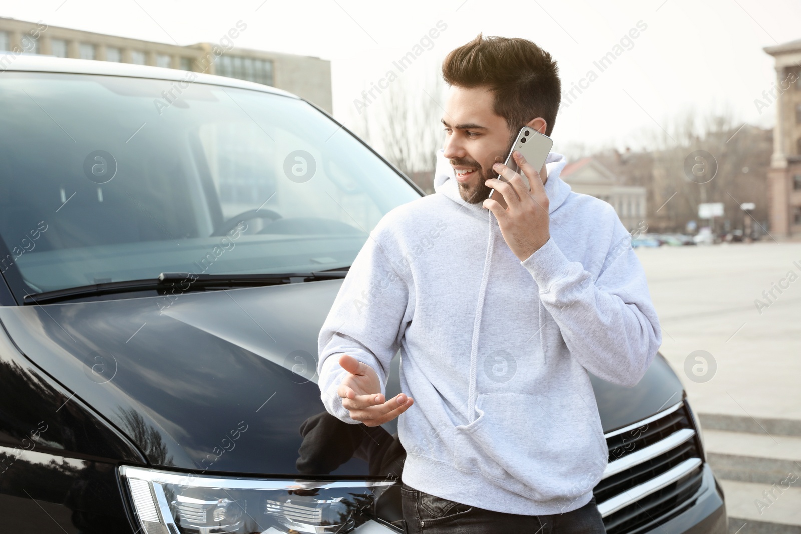 Photo of Handsome young man talking on phone near modern car outdoors