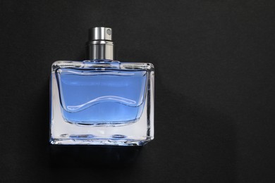 Blue men's perfume in bottle on black background, top view. Space for text