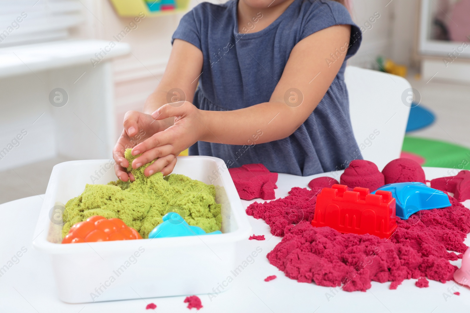 Photo of Little girl playing with bright kinetic sand at table indoors, closeup