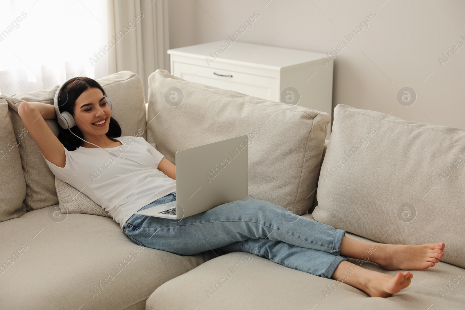 Photo of Woman with laptop and headphones lying on sofa at home