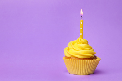 Photo of Delicious birthday cupcake with yellow cream and burning candle on violet background. Space for text