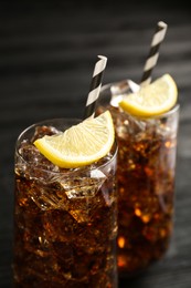 Glasses of refreshing soda water with ice cubes and lemon slices on black table, closeup