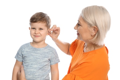 Photo of Mature woman putting hearing aid in little grandson's ear on white background