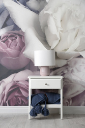 Photo of White nightstand near wall with floral wallpaper. Stylish room interior
