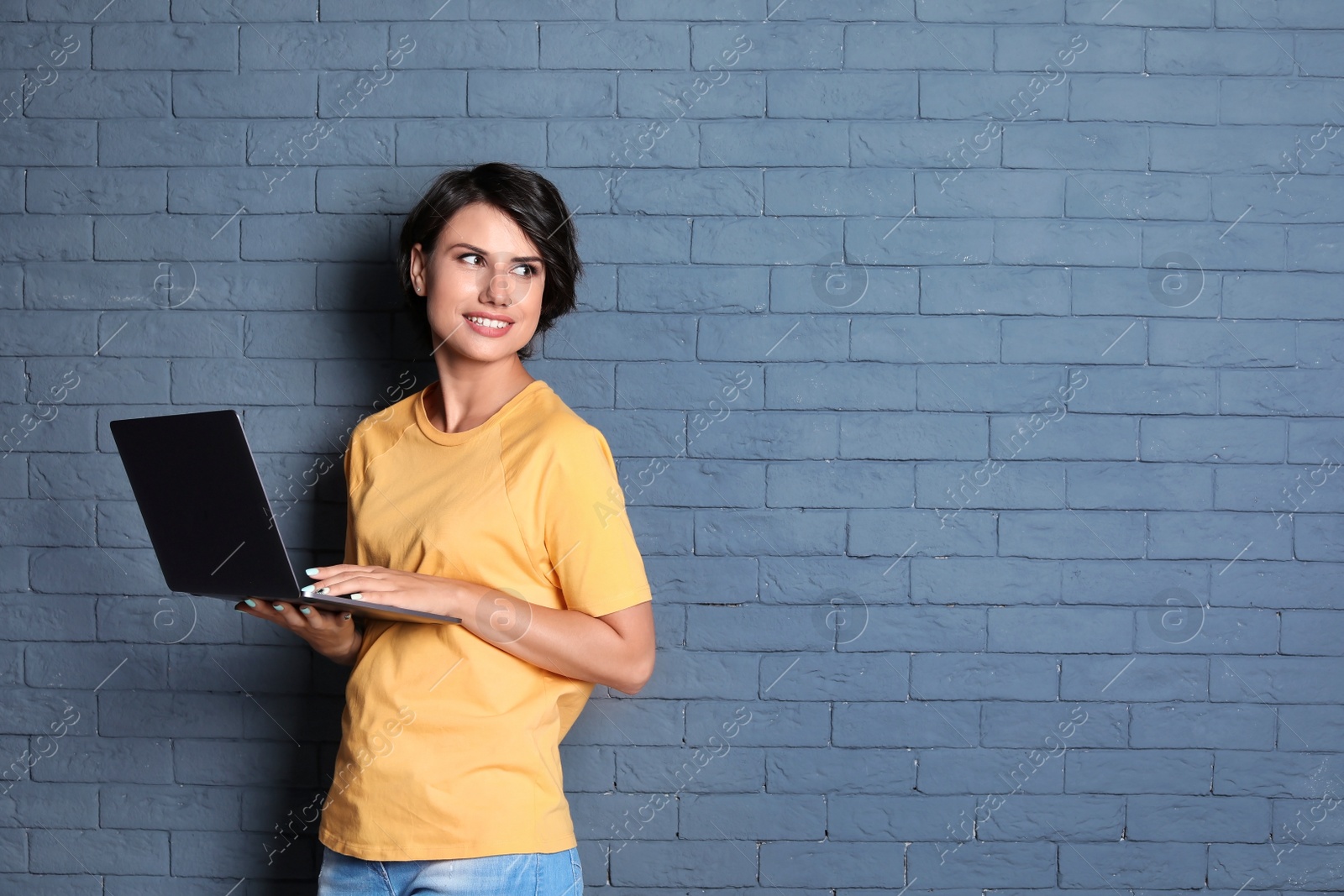 Photo of Young woman with modern laptop on brick wall background