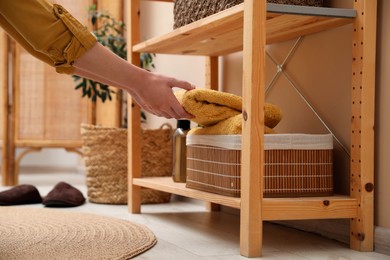 Woman putting towel into storage basket indoors, closeup