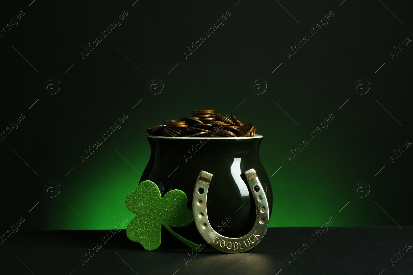 Photo of Pot with gold coins, horseshoe and clover on table against dark background. St. Patrick's Day