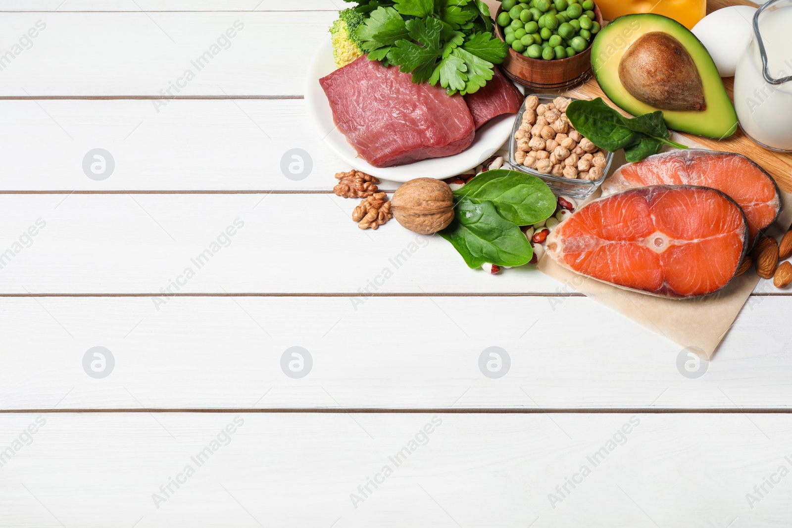 Photo of Different products rich in protein on white wooden table. Space for text