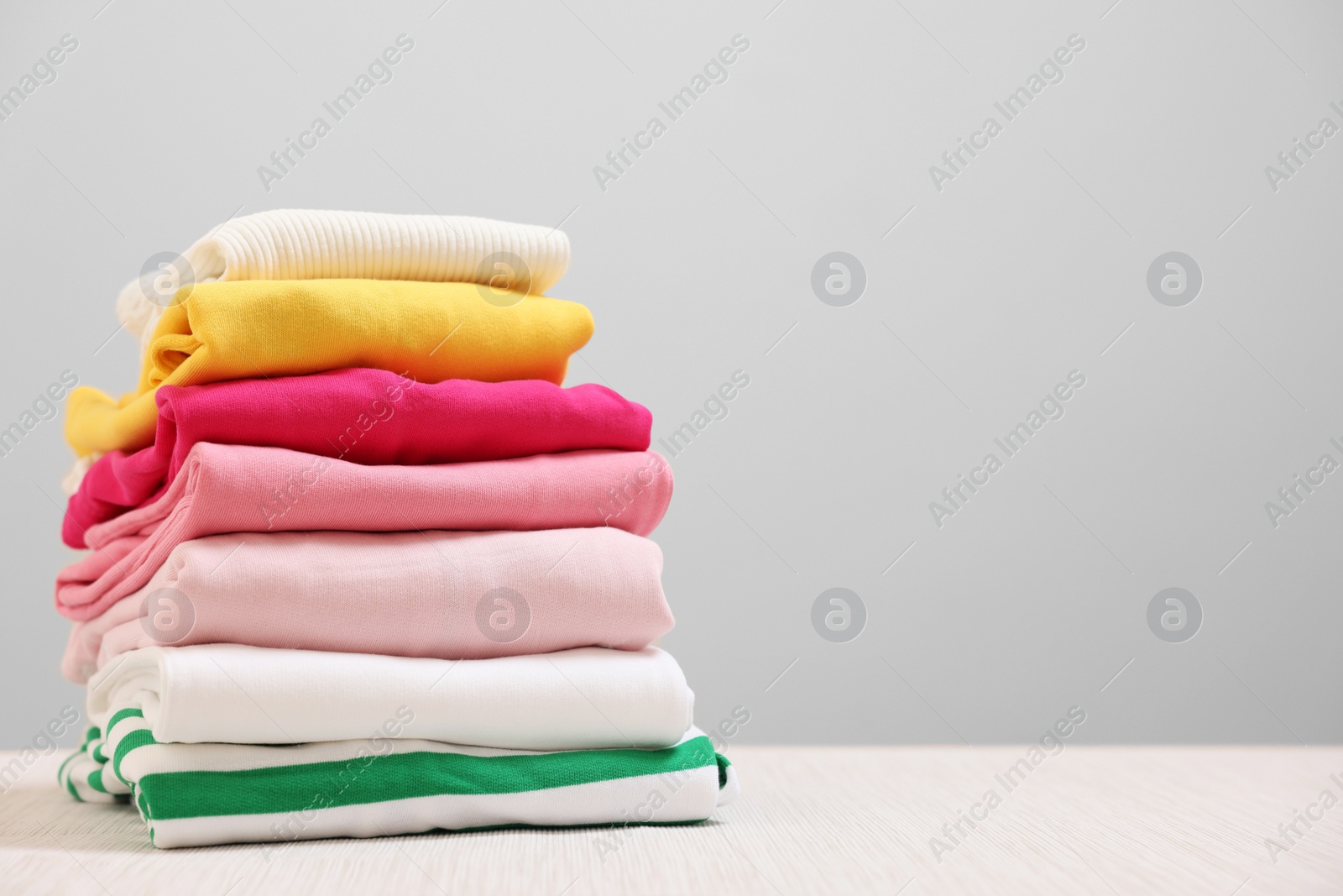Stack of folded clothes on wooden table against beige background, space for text Photo of Stack of folded clothes on wooden table against beige background, space for text