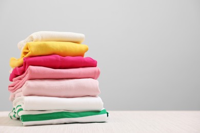 Photo of Stack of folded clothes on wooden table against beige background, space for text