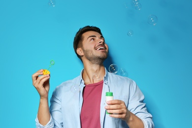 Young man blowing soap bubbles on color background