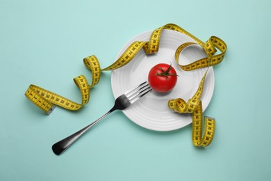 Plate, tomato, fork and measuring tape on turquoise background, top view. Diet concept