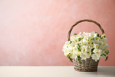 Photo of Beautiful freesia flowers in basket on white table. Space for text