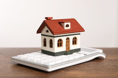 Photo of Mortgage concept. House model and calculator on wooden table against white background, closeup