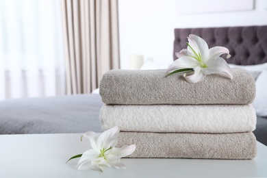 Photo of Stack of fresh towels with flowers on table in bedroom. Space for text