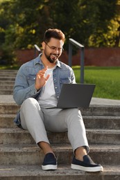 Photo of Handsome young man with laptop sitting on concrete stairs outdoors