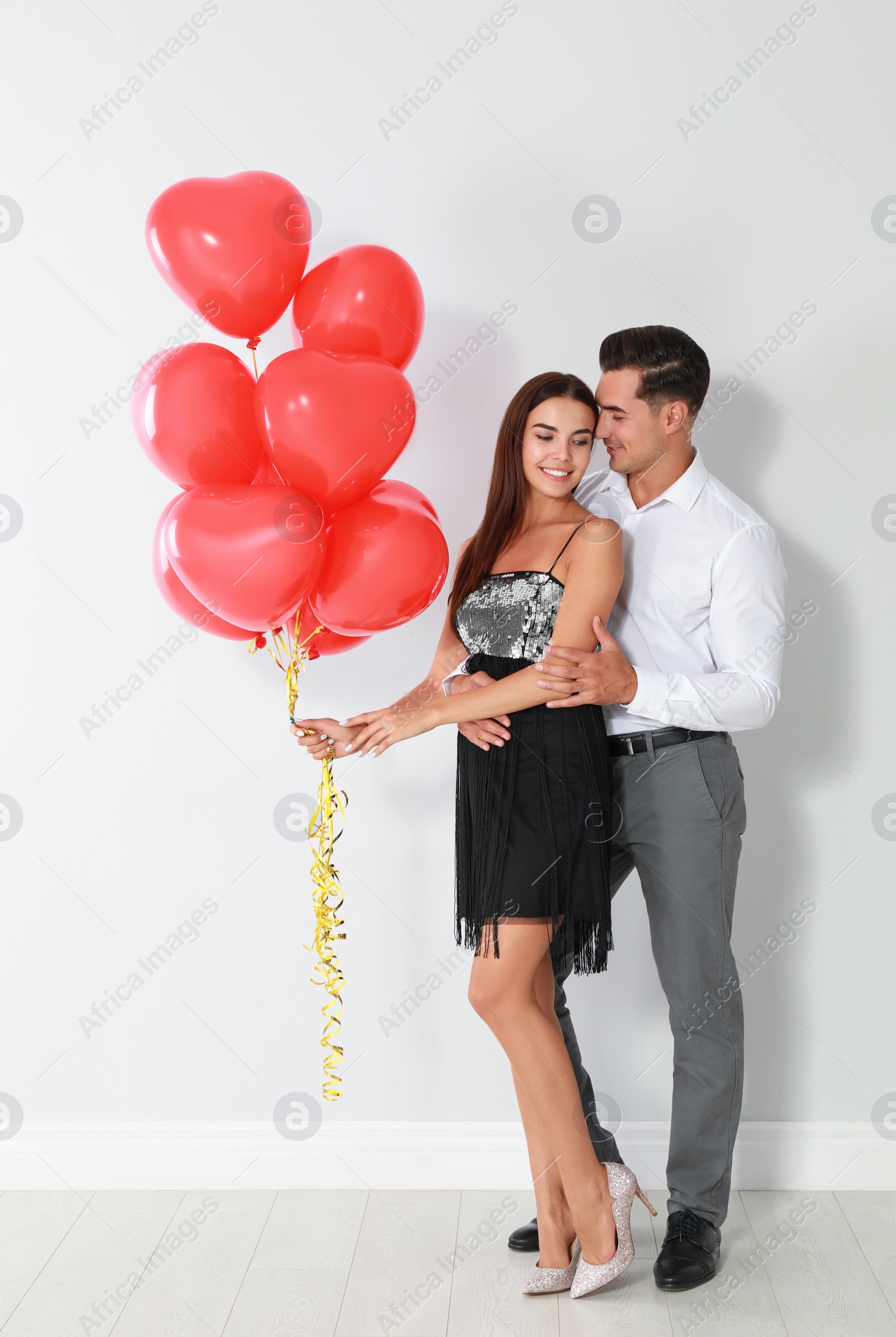 Photo of Beautiful couple with heart shaped balloons near light wall