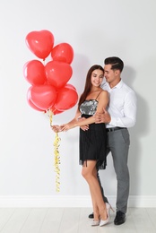 Photo of Beautiful couple with heart shaped balloons near light wall
