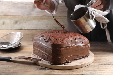 Woman pouring chocolate cream into homemade sponge cake at wooden table, closeup