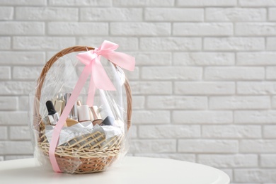 Photo of Wicker gift basket with cosmetic products on table near white brick wall. Space for text