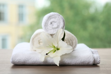 Photo of Pile of fresh towels and flower on table against blurred background