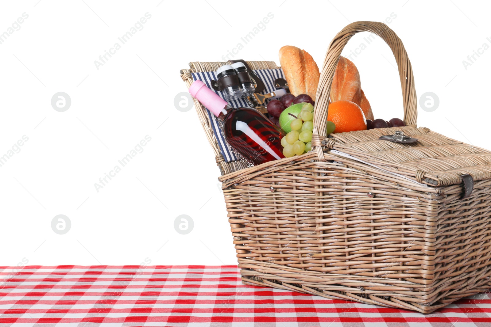 Photo of Wicker picnic basket with different products on checkered tablecloth against white background, space for text