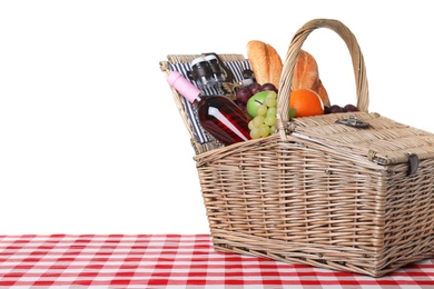 Photo of Wicker picnic basket with different products on checkered tablecloth against white background, space for text