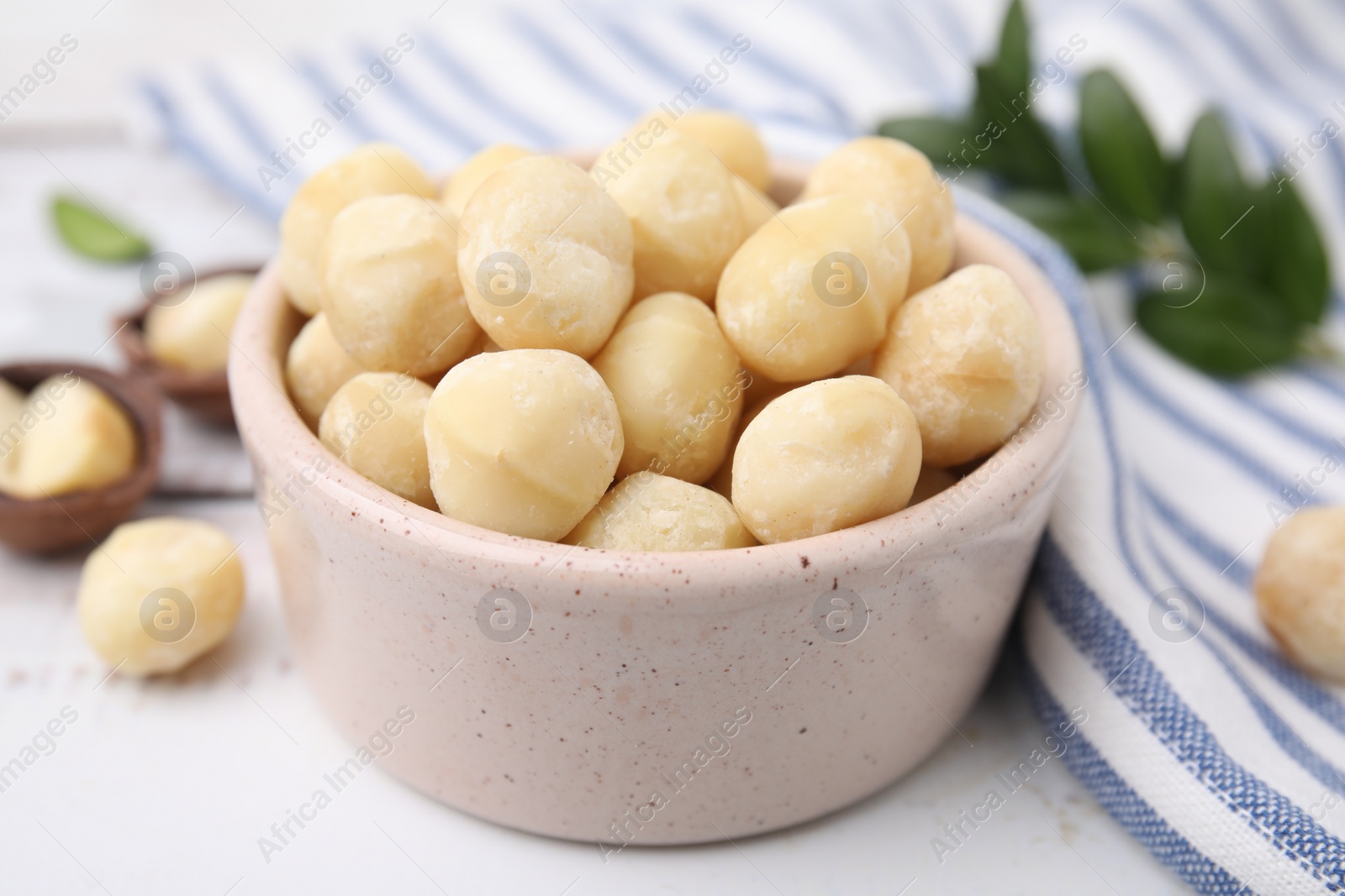 Photo of Tasty peeled Macadamia nuts in bowl on white table, closeup