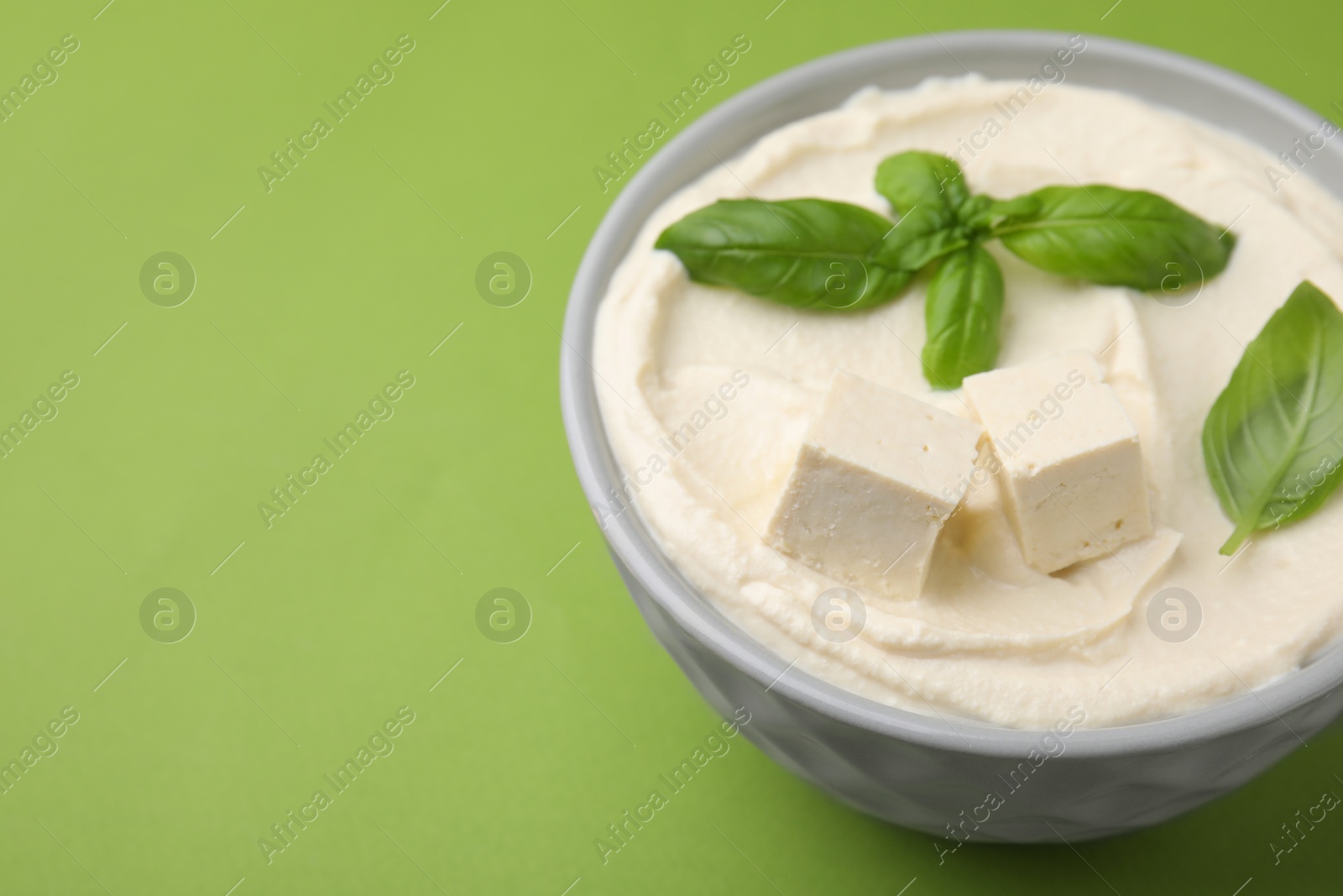 Photo of Delicious tofu sauce and basil leaves on green background, closeup. Space for text