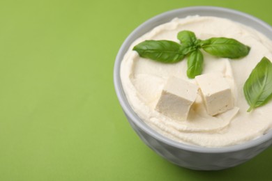 Delicious tofu sauce and basil leaves on green background, closeup. Space for text