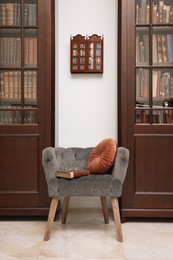 Photo of Comfortable armchair with pillow and book between wooden bookcases in library