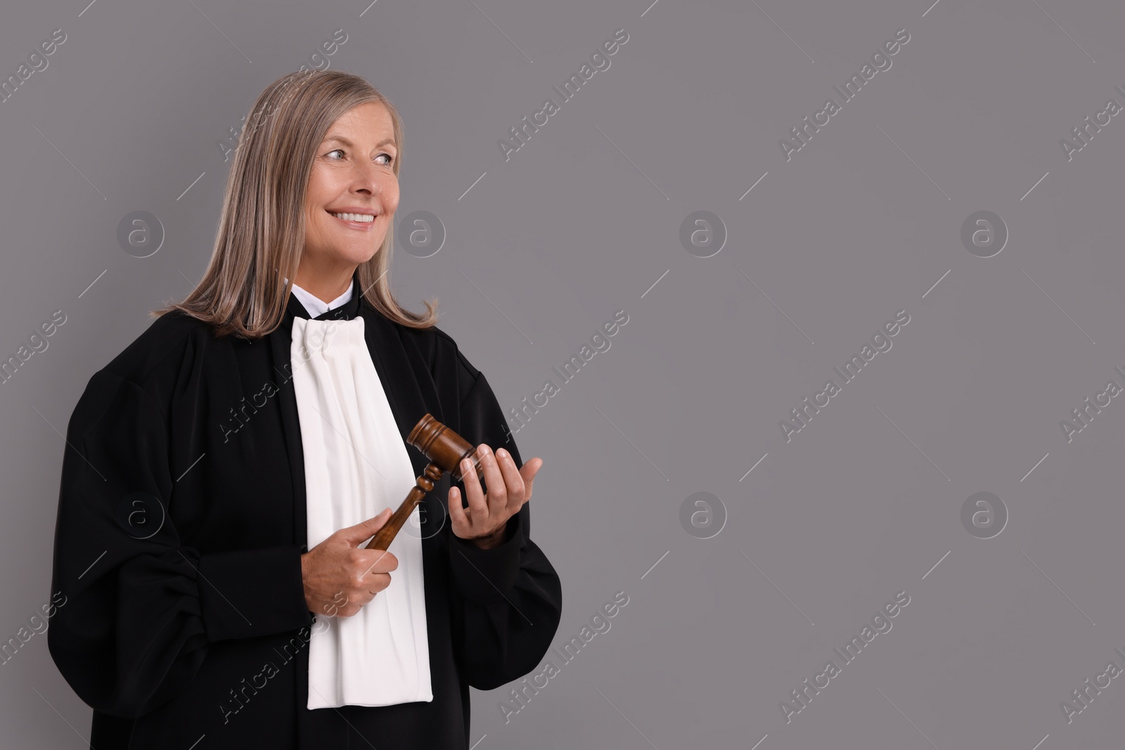 Photo of Smiling senior judge with gavel on grey background. Space for text