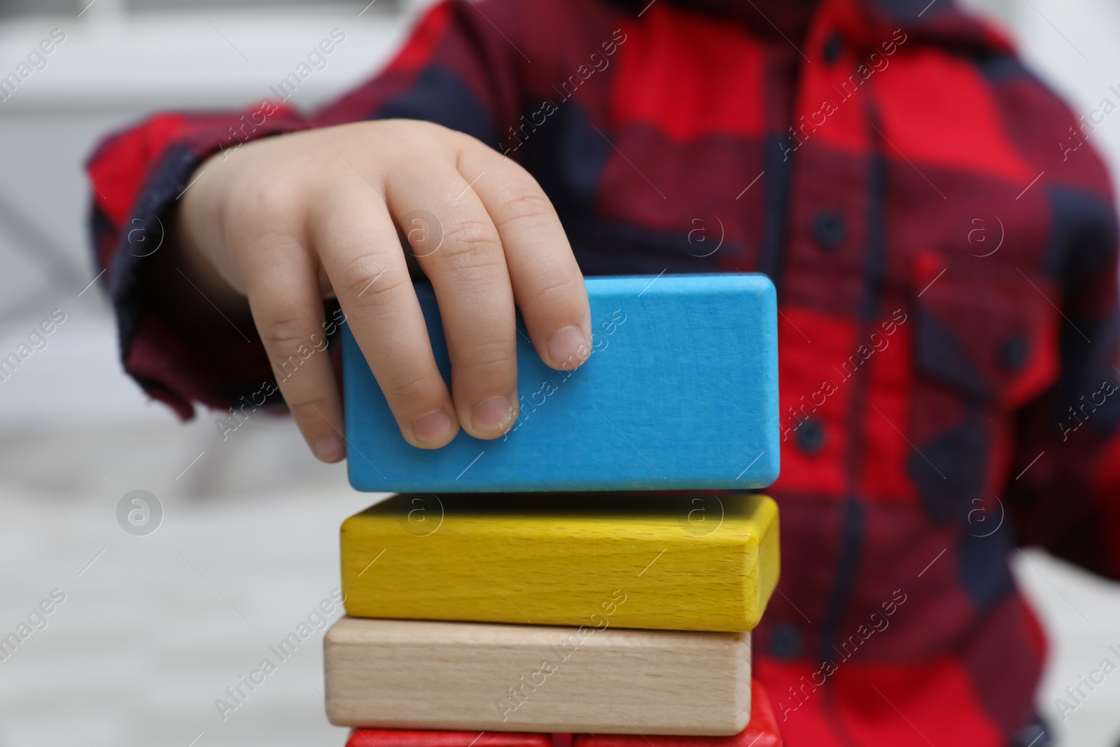 Photo of Little child playing with building blocks indoors, closeup