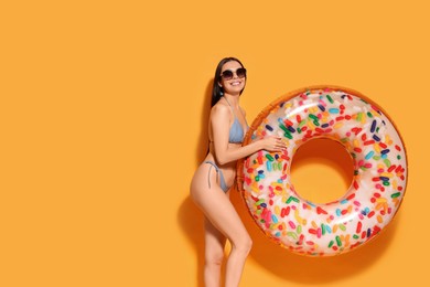 Photo of Young woman with stylish sunglasses holding inflatable ring against orange background. Space for text