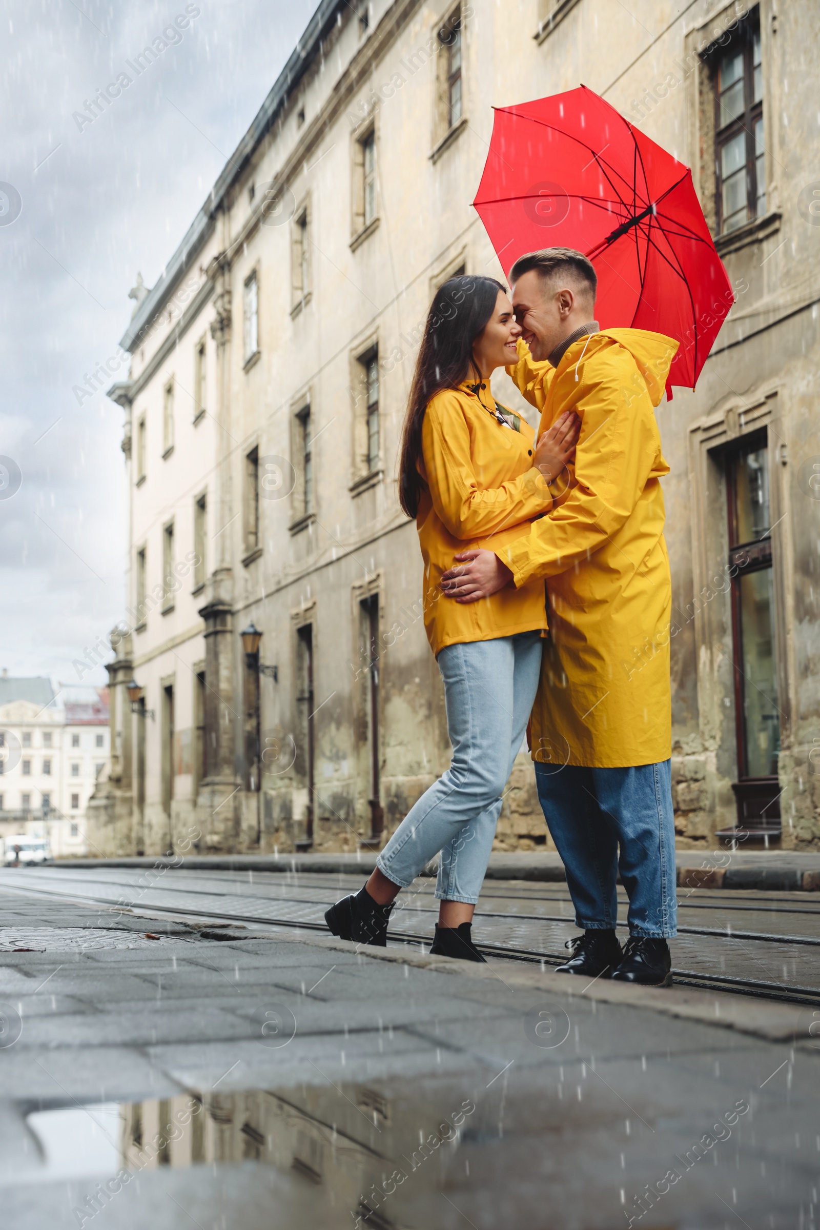 Photo of Lovely young couple with red umbrella together on city street