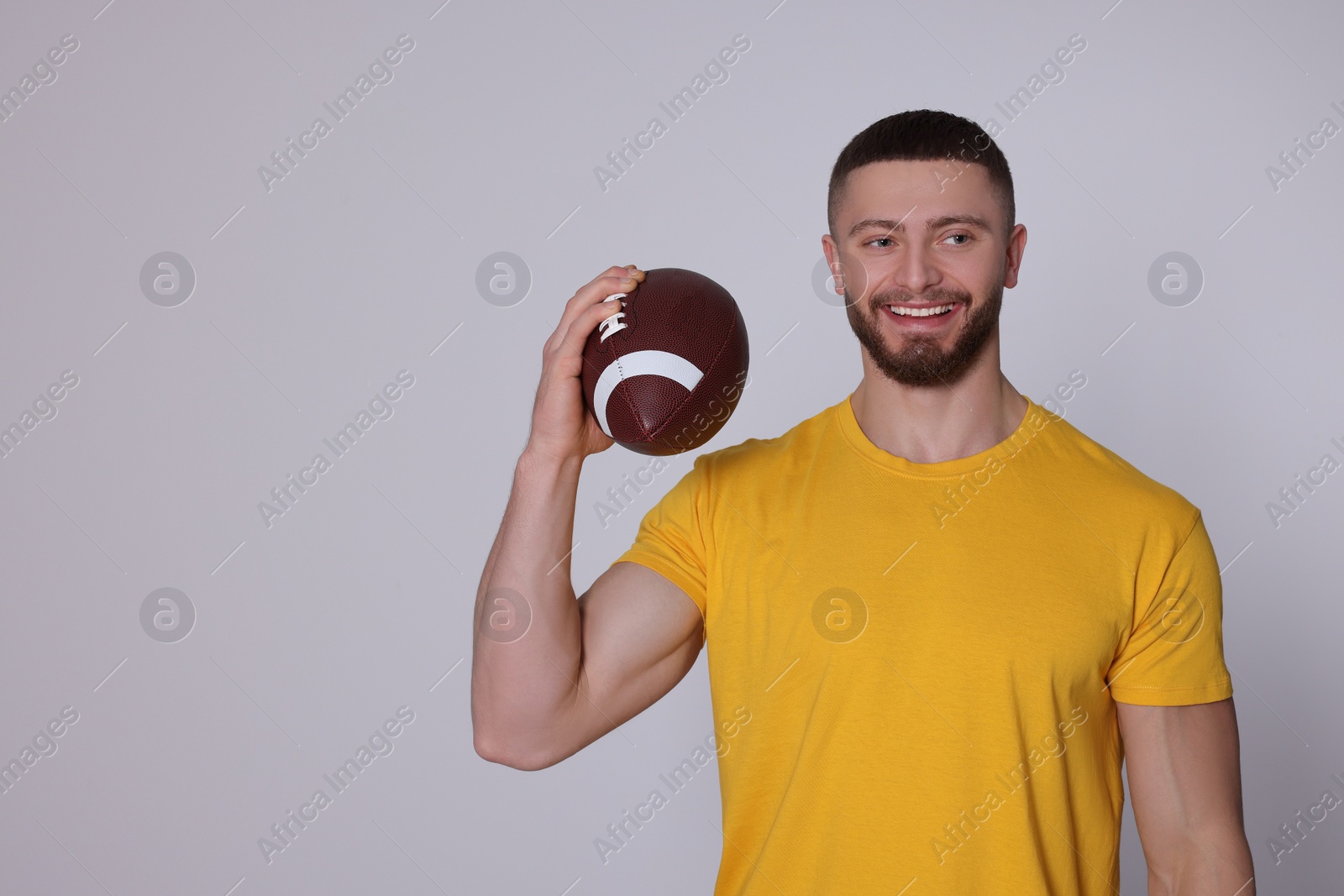 Photo of Athletic young man with American football ball on light grey background. Space for text