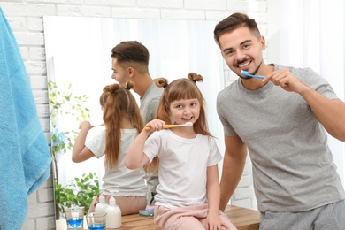 Photo of Little girl and her father brushing teeth together in bathroom at home