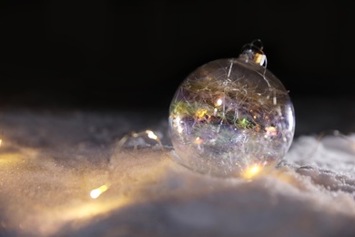 Photo of Christmas ball and fairy lights on white snow outdoors. Space for text