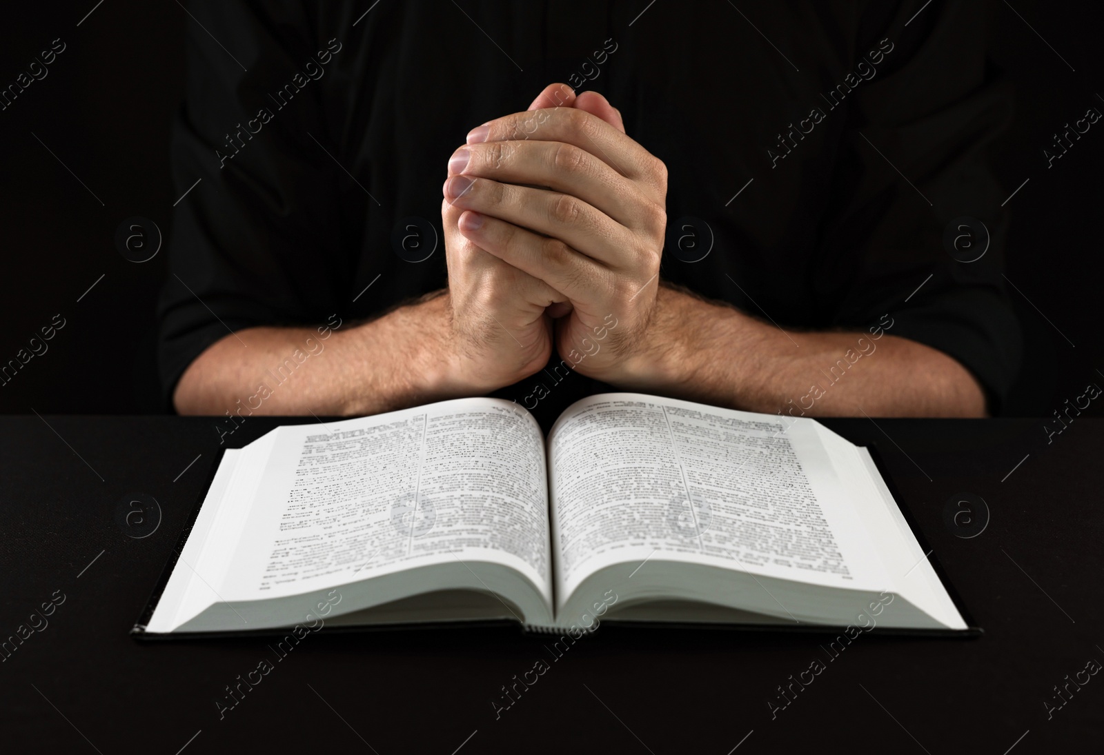 Photo of Man with Bible praying at black table, closeup