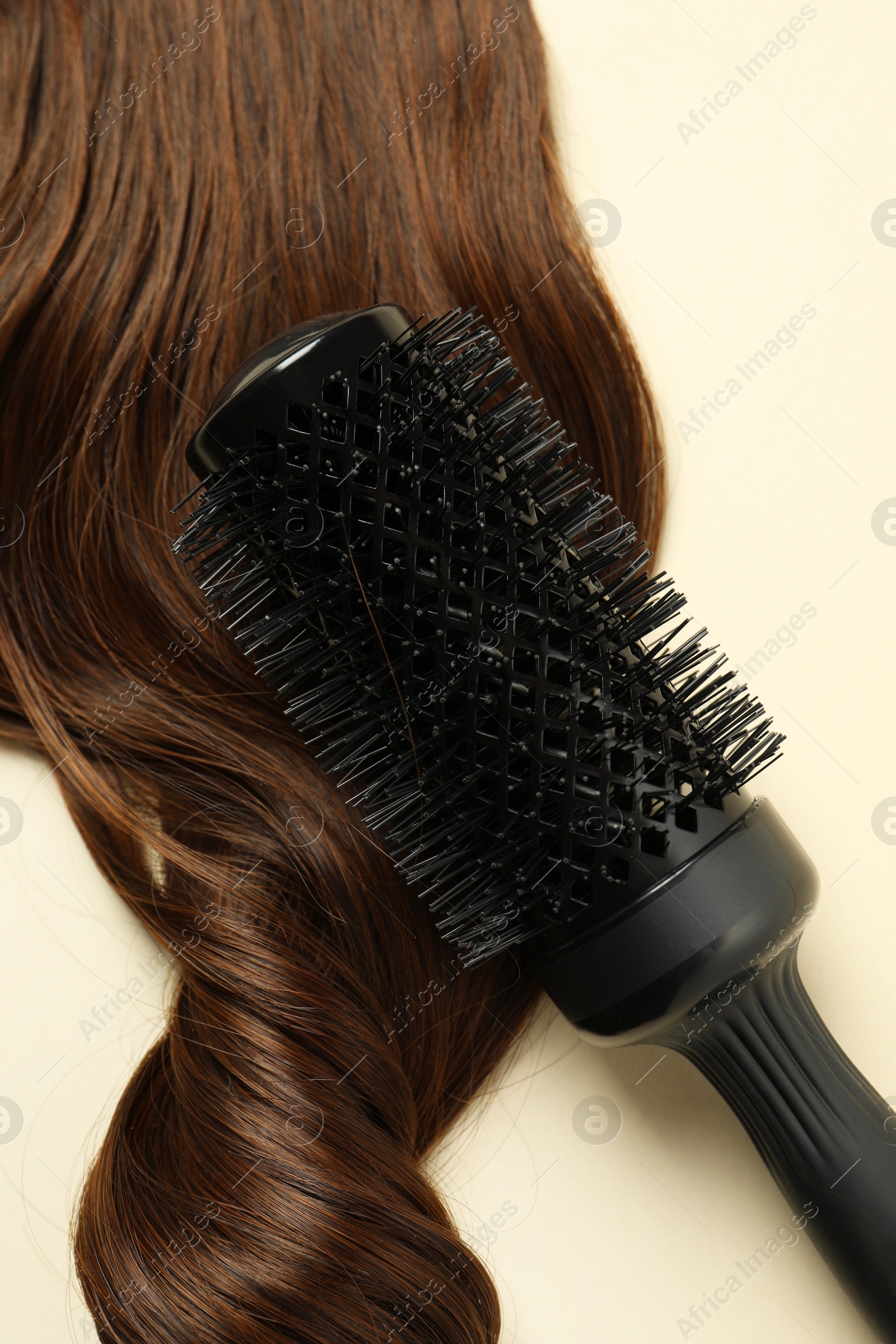 Photo of Professional round brush with brown hair strand on beige background, top view