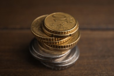 Many Euro coins stacked on wooden table, closeup
