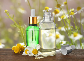 Bottles of essential oils and flowers on wooden table against blurred background