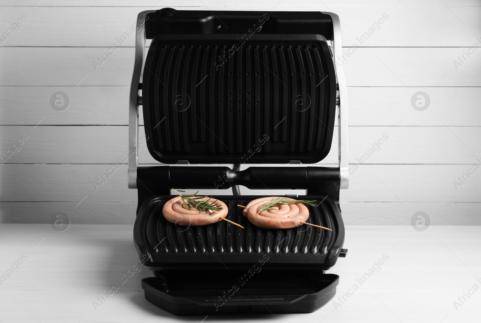 Photo of Electric grill with homemade sausages and rosemary on wooden table