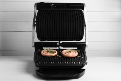 Electric grill with homemade sausages and rosemary on wooden table