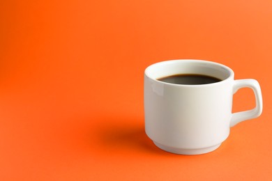 Photo of White mug of freshly brewed hot coffee on orange background, space for text