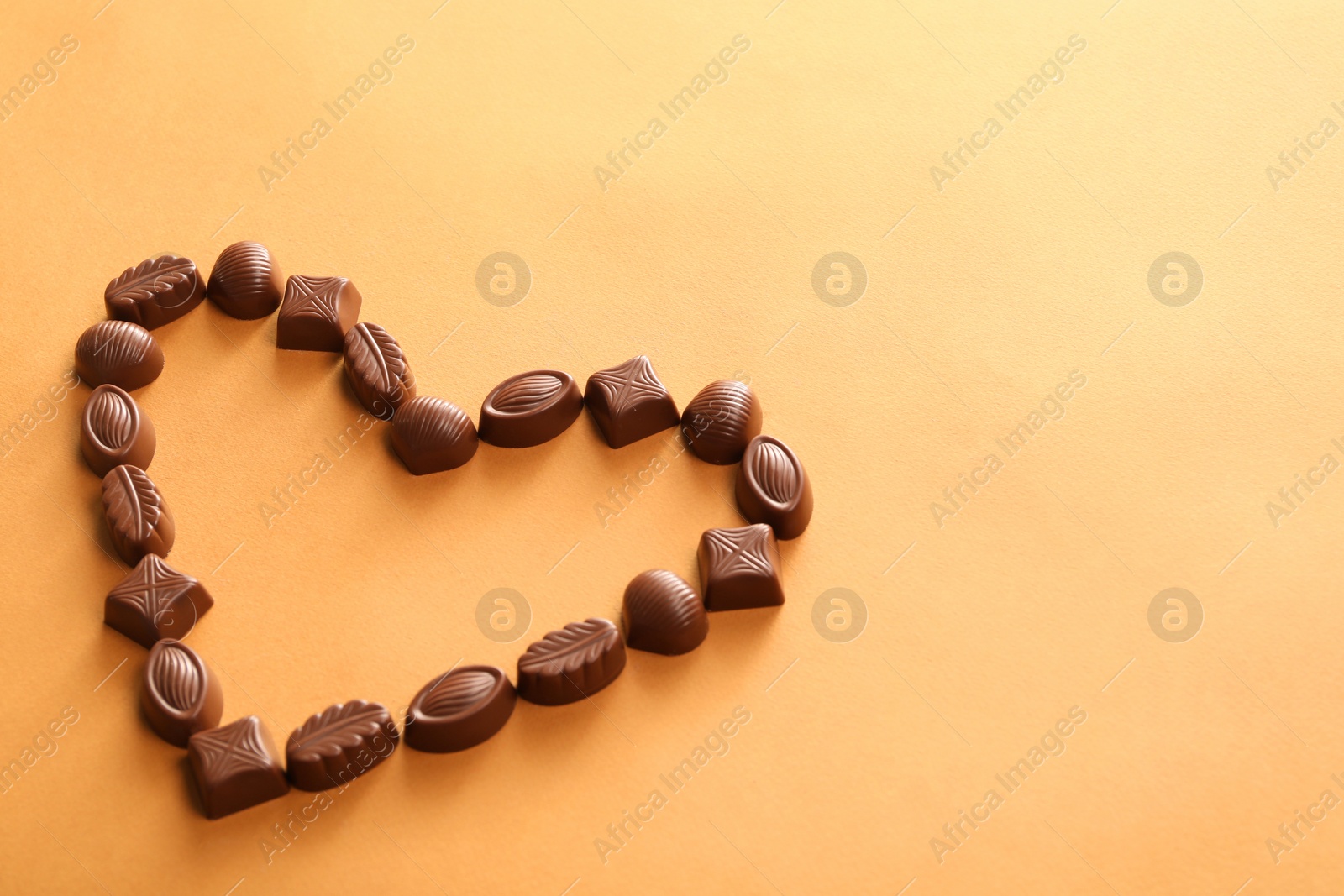 Photo of Heart made with delicious chocolate candies on brown background. Space for text