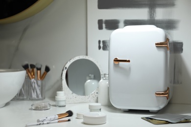 Photo of Cosmetics refrigerator and skin care products on white table indoors