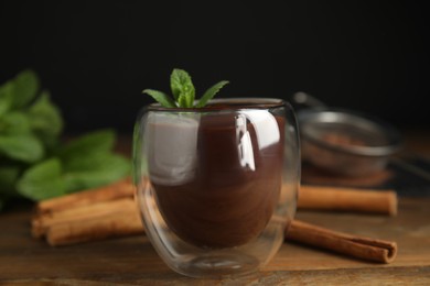 Photo of Glass of delicious hot chocolate with fresh mint and cinnamon sticks on wooden table